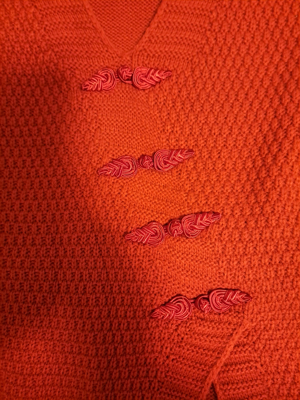 knitted red vest with four decorative frog closures. This garment has a tex